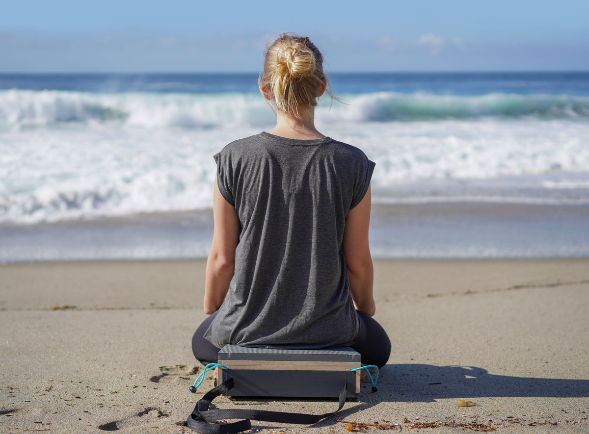 A woman practicing seated meditation on a Mindtra bench beside a forest stream.